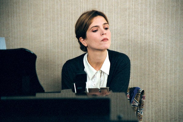 Femme en costume (Agnès Jaoui), assise derrière un bureau, regardant vers le bas en faisant la moue